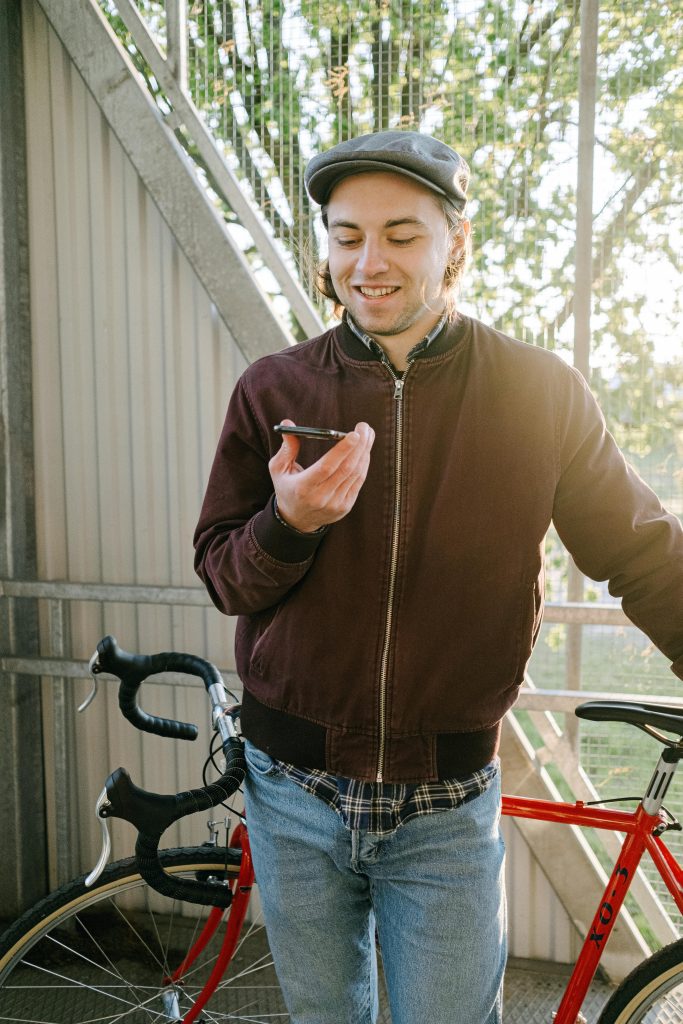 zipwp-image-4828923 Smiling young man holding smartphone next to red bicycle outdoors.